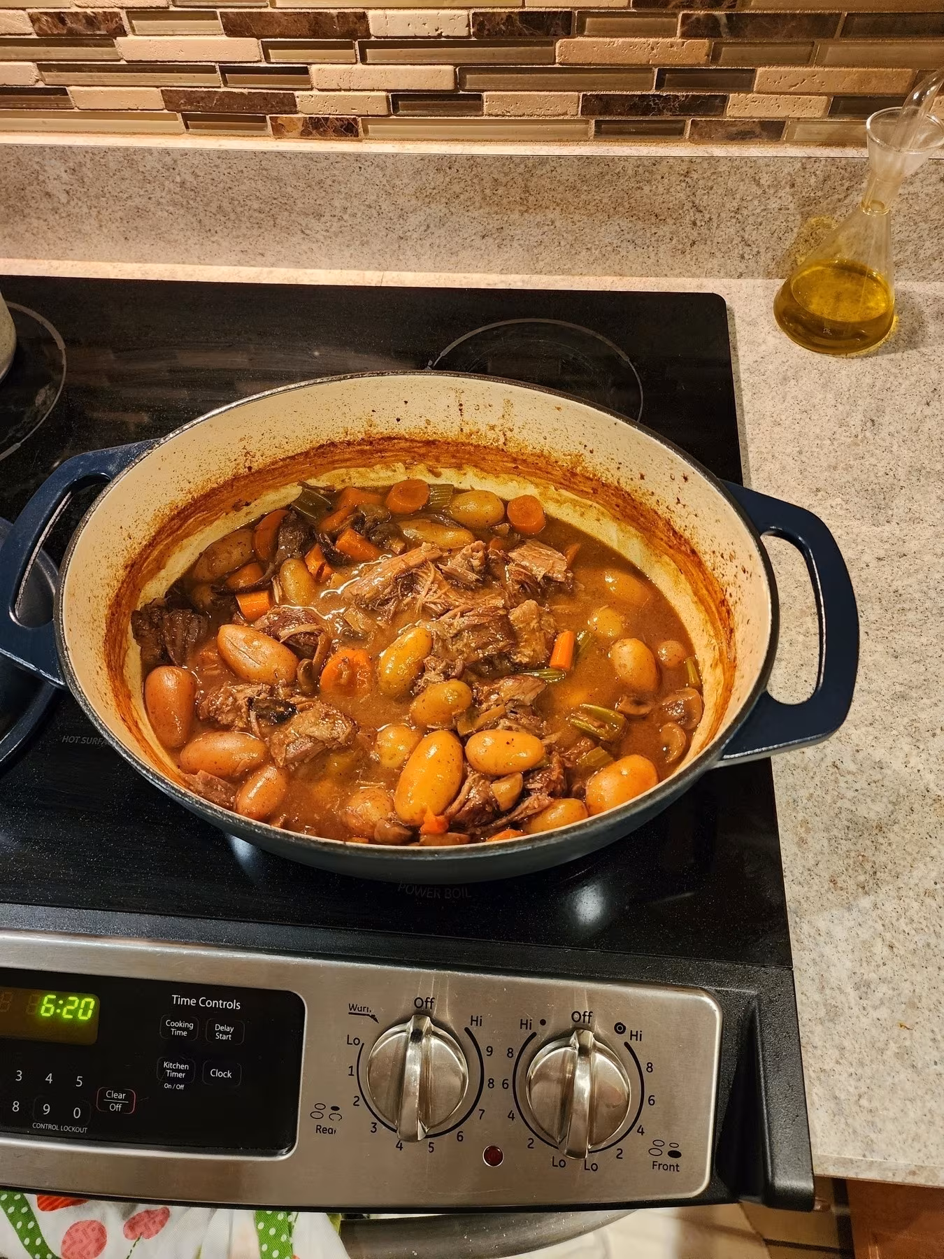 A pot of beef stew containing chunks of meat, potatoes, and carrots simmers on a stovetop.