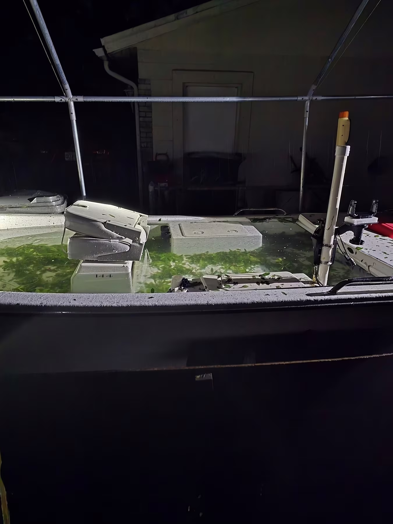 A flooded boat filled with water is seen at night, situated next to a house or building.