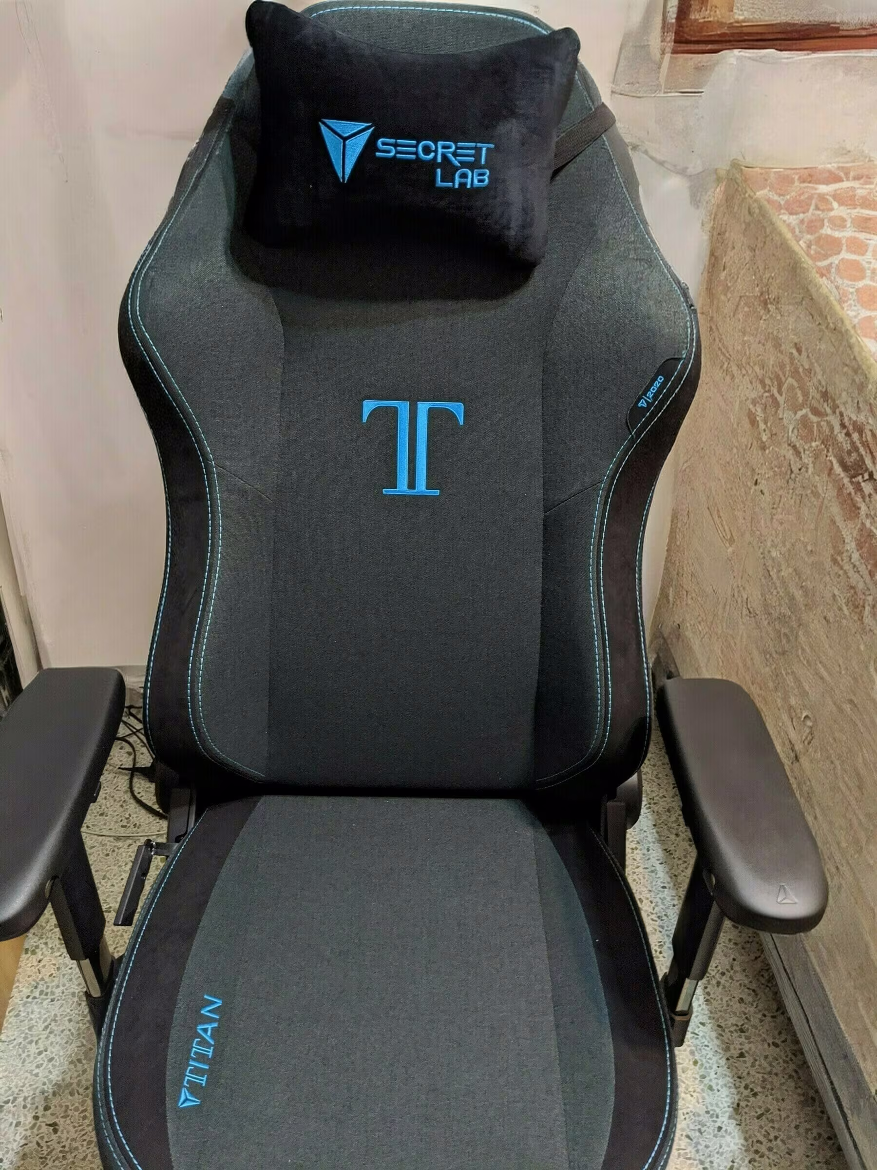 Auto-generated description: A Secretlab Titan gaming chair with dark upholstery and blue accents is positioned in a corner.