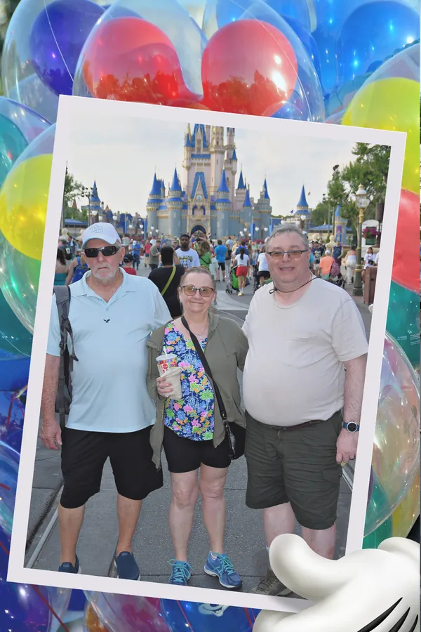 Three people posing in front of Cinderella Castle framed by colorful Disney balloons