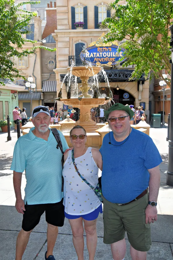 Three people posing at the France pavilion fountain with the Ratatouille Adventure sign visible