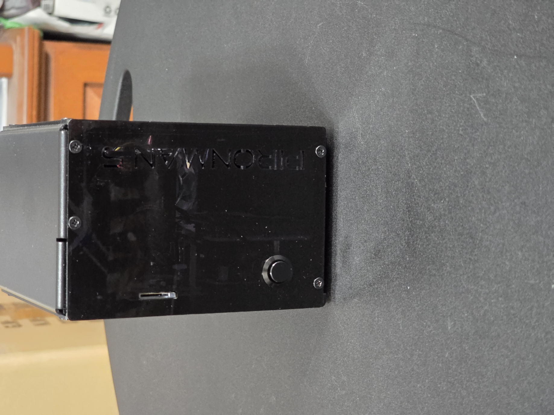 A black, vertical standing computer case with a glossy finish and the word "PIRONMAN" embossed on the front, placed on a textured gray surface. The case features visible ports and a power button on the front panel.